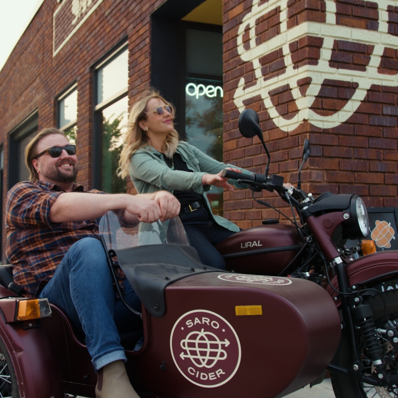 Woman driving the saro cider motorcylce with man in the sidecar